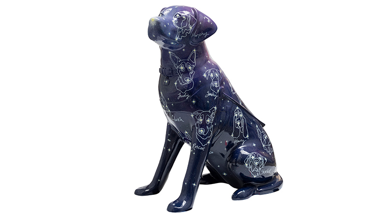 A purple guide dog sculpture covered with stars and constellations of other dogs who were former guide dogs. Their names are written beside each constellation.