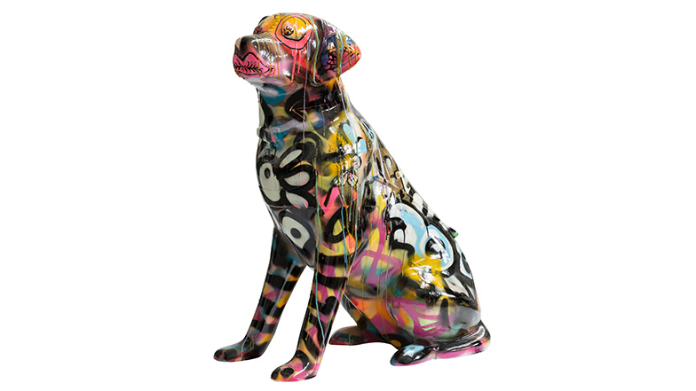 A multicoloured spray painted guide dog sculpture, covered in paint drips, and graffitied motifs such as a heart, lips and butterflies.