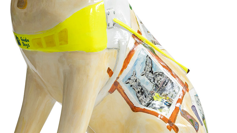Side view of the sculpture showing the white and high vis harness and a painted postcard on the dogs side.
