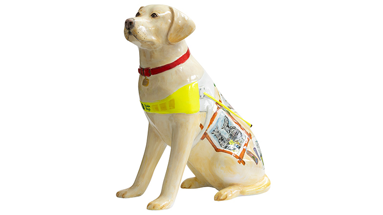 A realistic yellow guide dog sculpture with a white Guide Dogs harness. On the dog's back are postcards of guide dogs and their owners from different parts of the UK.