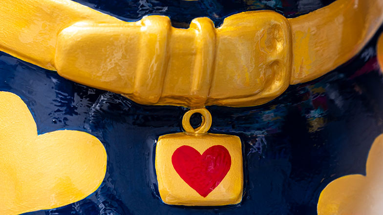 Close up of the sculpture's collar which is gold with a red heart tag. The chest is dark blue with gold hearts.