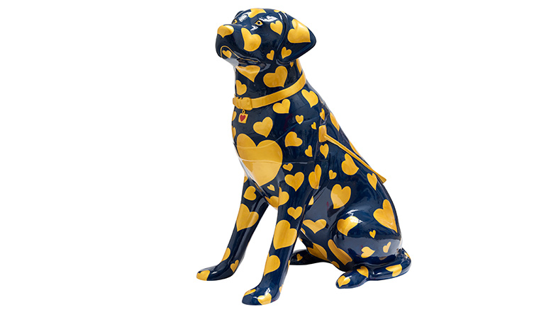 A guide dog sculpture with a dark blue background, covered in different sized golden hearts.