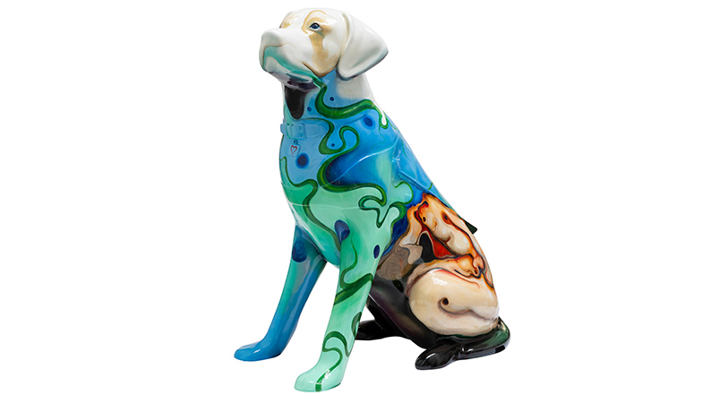A guide dog sculpture with an abstract painting on its hind legs of a person bending over their knees, but being held up by small figures. There is a person's face on the dog's back and they are holding out a hand. The dog has blue, green and grey swirls on its upper body. 