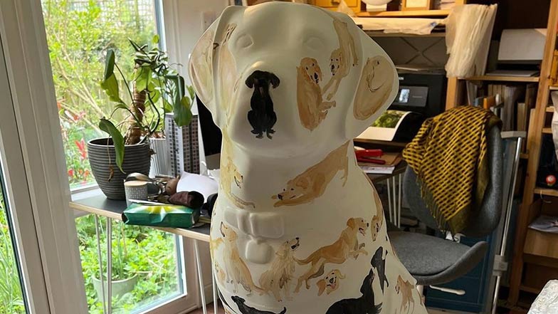 Head and shoulders of a white guide dog mini sculpture with small yellow and black Labradors and golden retrievers painted all over