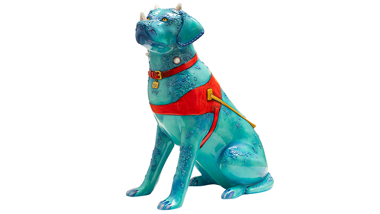 A guide dog sculpture that looks like a green dinosaur with textured scales and has horns growing out of its nose, ears and neck. The dog has a red collar and red and gold harness with yellow eyes.