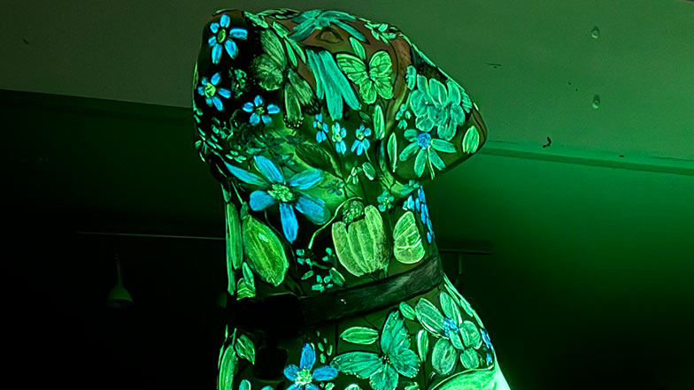 Close up of the head and chest of the sculpture with the lights turned off, showing the flowers and nature features glowing in the dark.