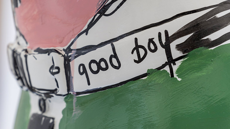 Close up of the sculpture's collar which is white and black with the words 'good boy' painted on.
