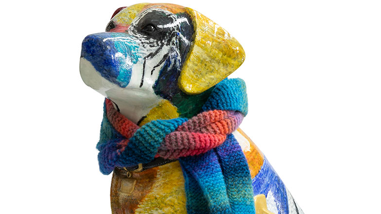 Head and shoulders of a sculpture painted in a multi-coloured knitted patchwork. It has a knitted scarf around its neck.