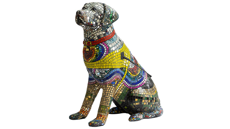 A guide dog sculpture covered in small tiles making a mosaic. The dogs chest is covered in multicoloured tiles that form a heart that then spreads out across it's shoulders. 