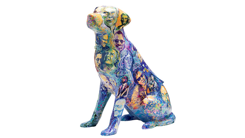 A guide dog sculpture covered with different faces of famous people past and present with lived experience of sight loss. Some of the people include Judith E. Heumann, Dr Abraham Nemeth, Claude Monet and Ray Charles.