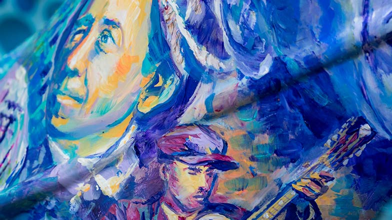 Close up of the sculpture's side which is decorated in a blue and purple painterly style showing a picture of various famous people with sight loss.