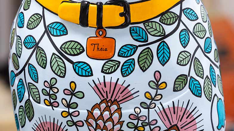 Close up of sculpture's chest which is pale blue with plants and thistles painted on. It has a yellow collar with an orange tag that reads 'Theia'.