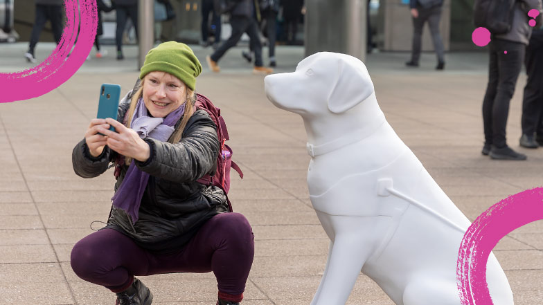 Lady crouching down taking a selfie photo of herself with the blank white guide dog sculpture