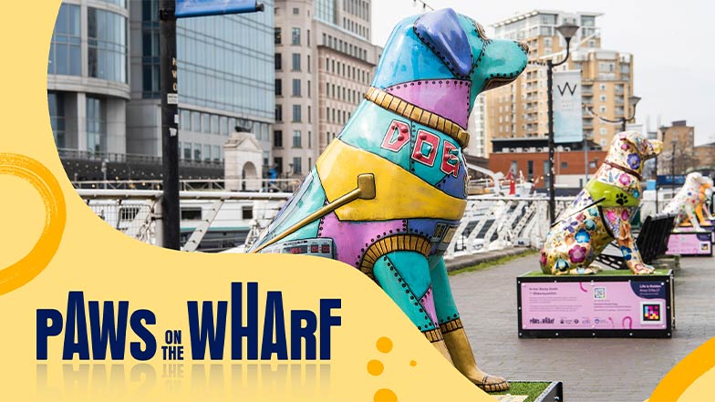 An image of colourful guide dog sculptures along the pavement of Canary Wharf. Over the top of the image is a yellow graphic with blue text which says 'Paws on the Wharf'.