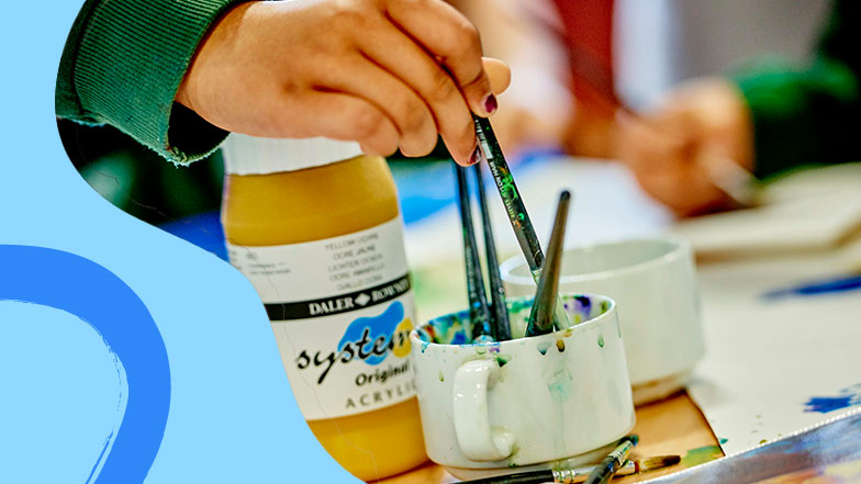 Close up of a school child's hand washing a paint brush in a cup ready to paint.