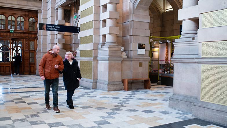 A man guides a lady through a museum entrance hallway