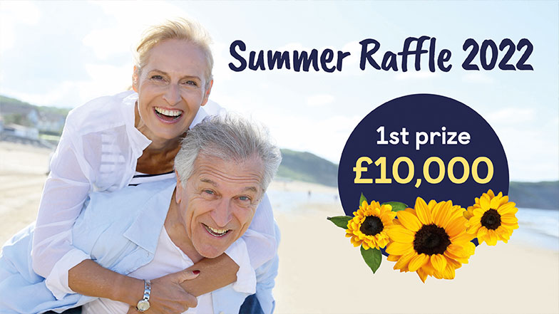 A couple on a beach looking towards camera with 1st prize bubble of £10,000