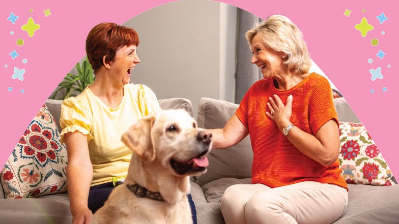 Two women on a couch smiling excitedly with a guide dog sitting in front of them