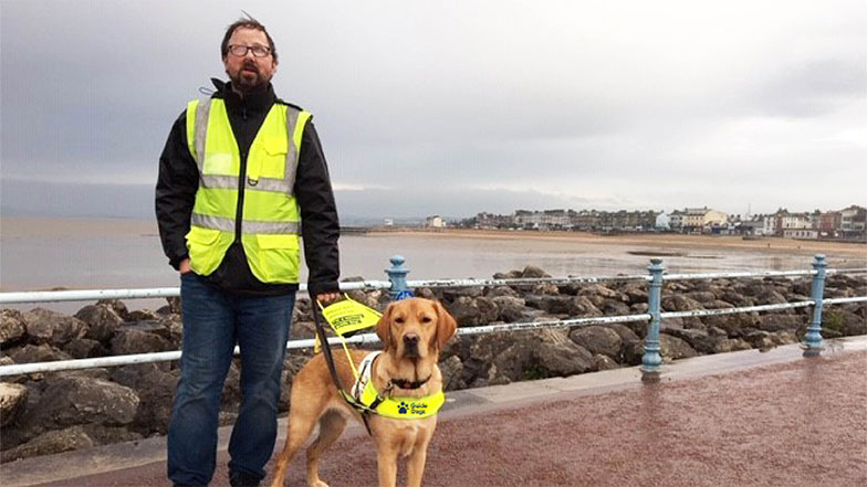 Guide dog owner Richard with guide dog Martin standing together on a sea front promenade