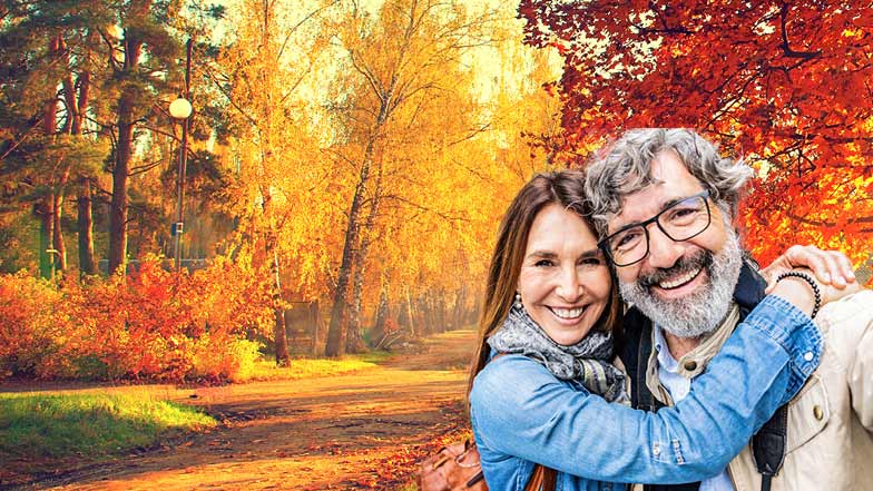 Smiling couple taking a selfie with autumn coloured trees in the background.