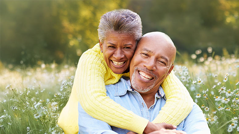 A couple hugging and smiling sitting together in a field of daisies.