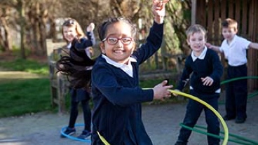 A young school girl plays with a hula hoop while other children watch her