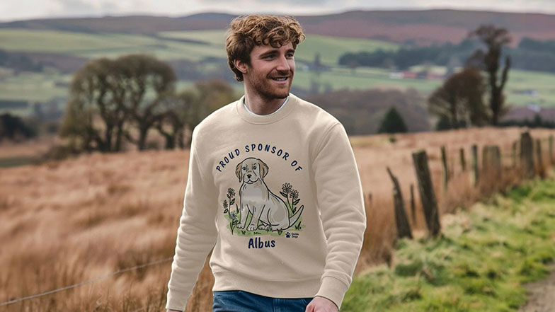 Smiling man walking in the countryside wearing a sweatshirt with sponsored pup Albus design.