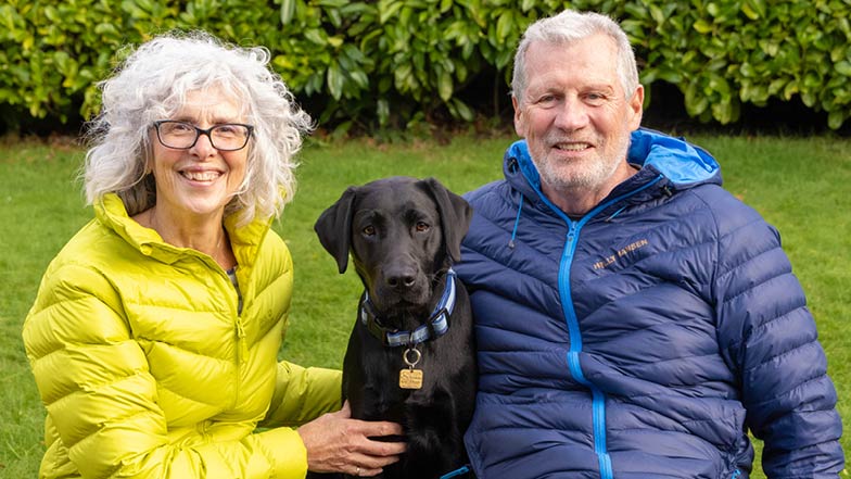 Sage sat between Puppy Raisers Chrisi and Colin looking into camera Sage sat between Puppy Raisers Chrisi and Colin looking into camera