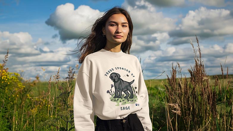 Woman in the countryside wearing a sweatshirt with sponsored pup Sage design.