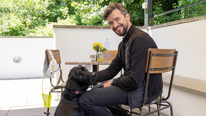 Guide dog owner with his guide dog sitting outside at a café.