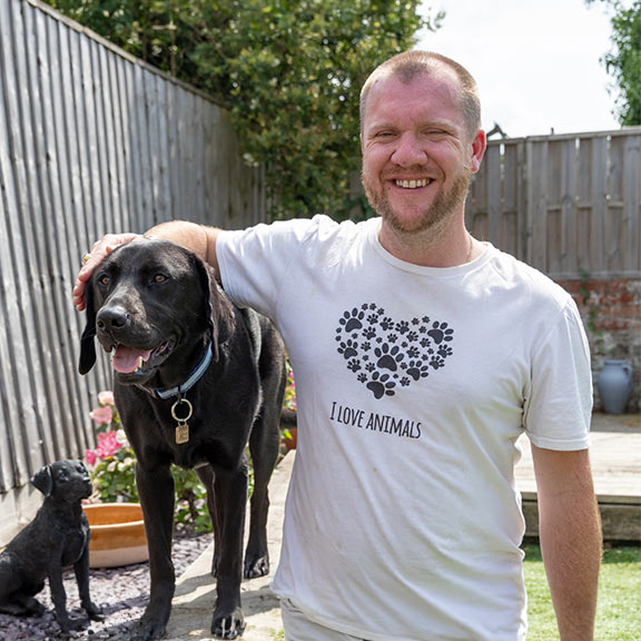 A smiling James and guide dog Comet standing together in the garden
