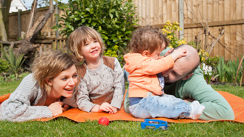 Family in a garden lying down on a mat and playing Guide Dogs