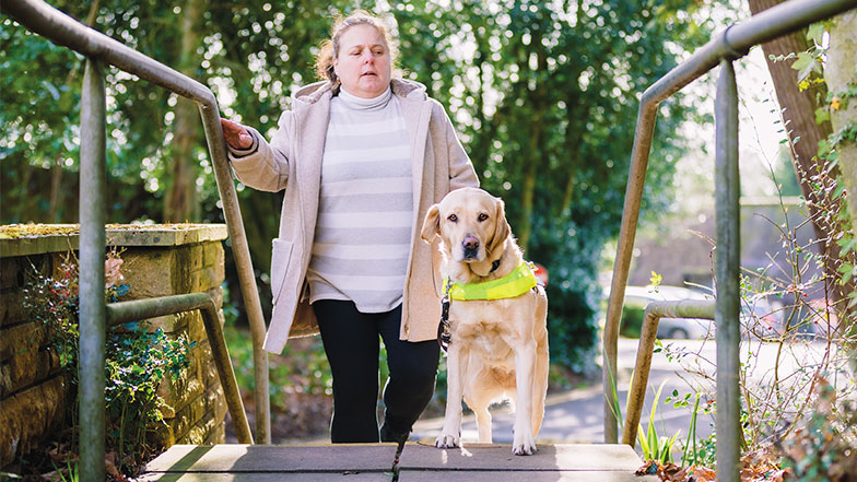 A lady with vision impairment walking up some steps while being guided by her guide dog.