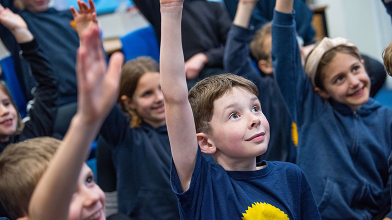 Kids at school raising their hands eager to answer a question about Guide Dogs.