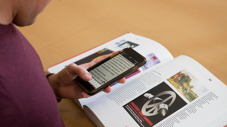 Guide Dogs service user using magnifying app on phone to read a textbook