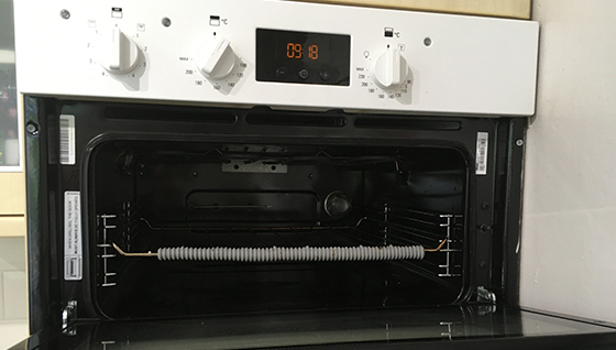 Image shows an oven cavity with an open door, the shelf has a grey shelf guard. 