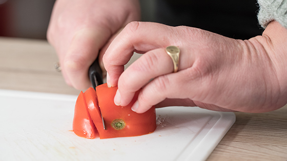 Person chopping tomato with fingers tucked