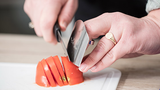 An image of someone chopping a tomato using a finger guard