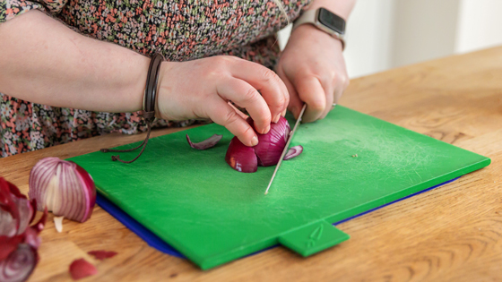 A woman slicing a red onion on a red chopping board