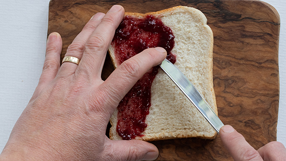 Someone using the bridge technique to spread jam onto a piece of bread