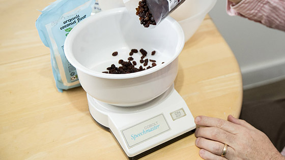 Someone pouring some raisins into a set of talking scales 
