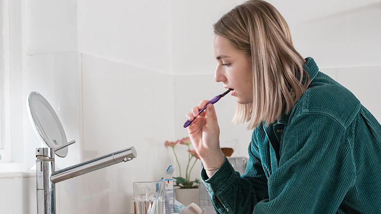 Women brushing her teeth in front of a mirror