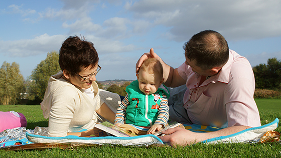 Parents with baby reading on a mat outside