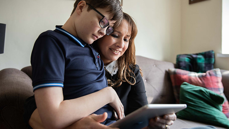 Boy sitting with his mum looking at an iPad screen together and smiling