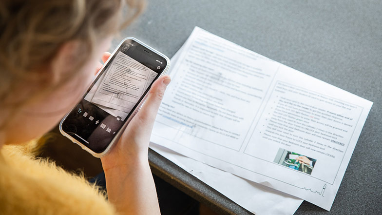 A woman holding an iPhone to a piece of paper with text on to read it with the Seeing AI app