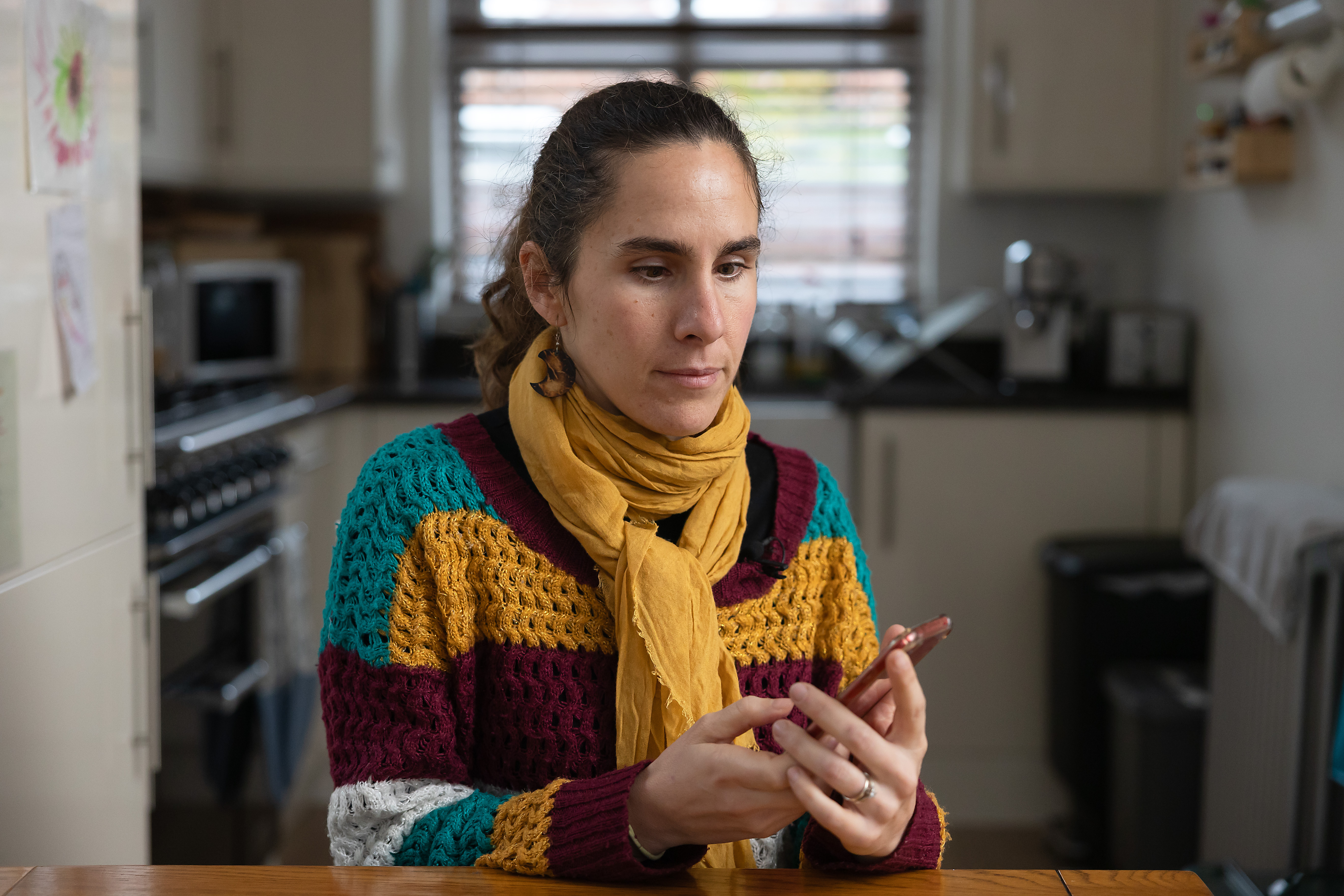 Alba, who has sight loss, uses apps on her smartphone at her kitchen table. 