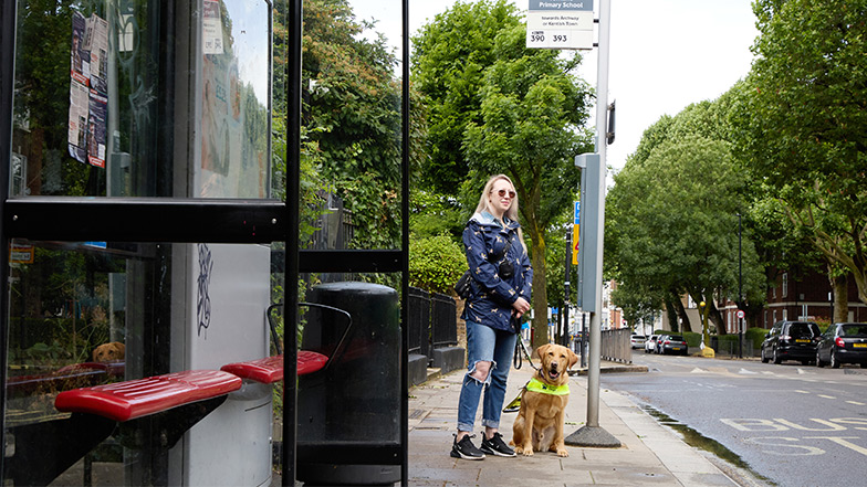 Guide dogs owner Emma stands at a bus stop with guide dog Archie