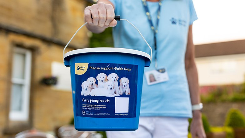A Guide Dog's volunteer holds out a branded collection box in front of her