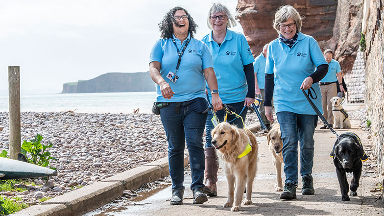 Group of volunteer fundraisers walk along a coastal path with guide dogs