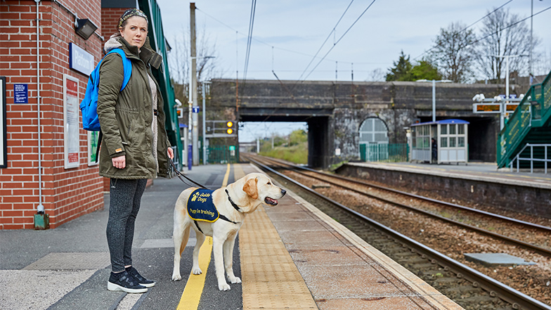volunteer puppy raiser stands at train station with puppy